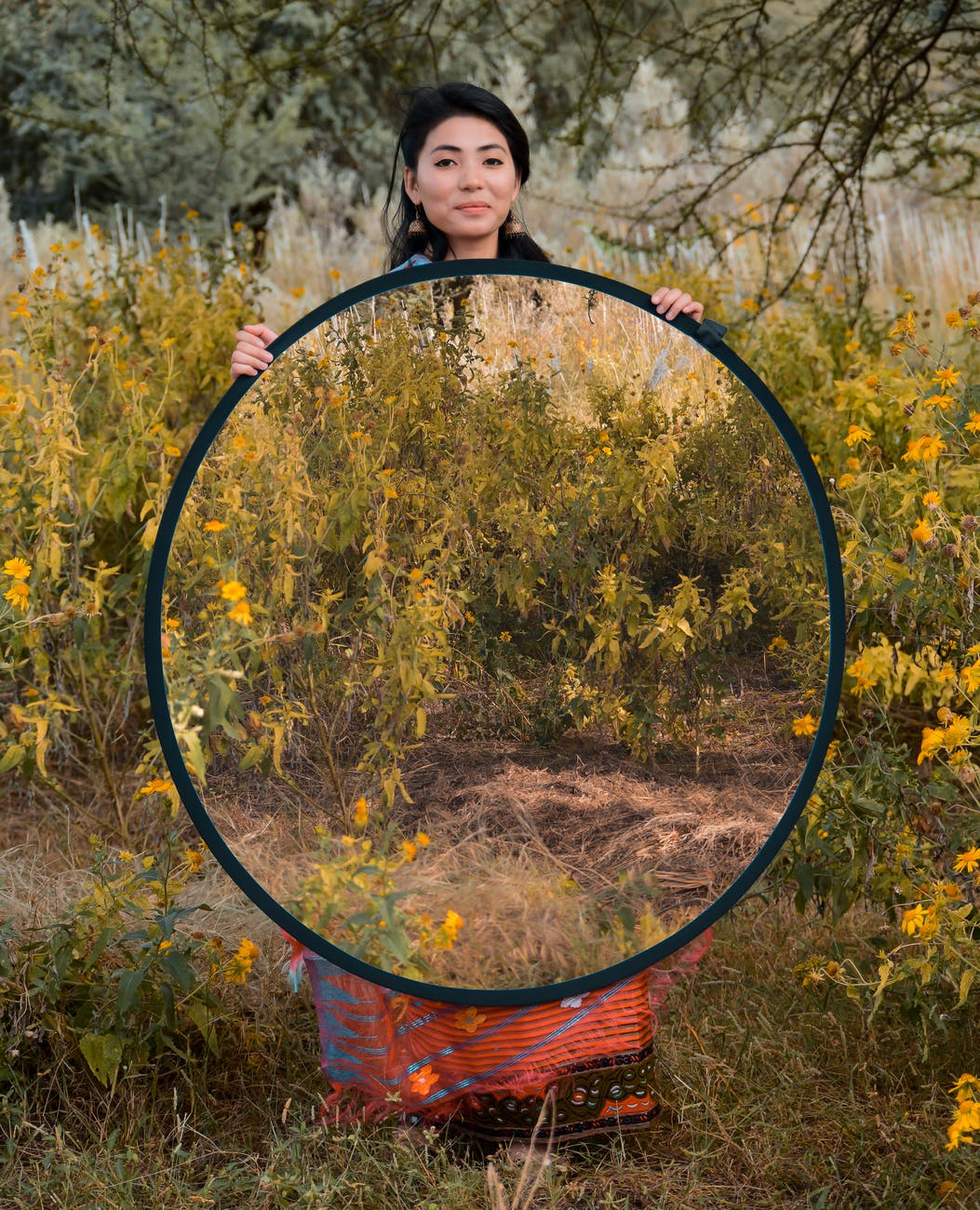 smiling ethnic woman with big mirror in nature